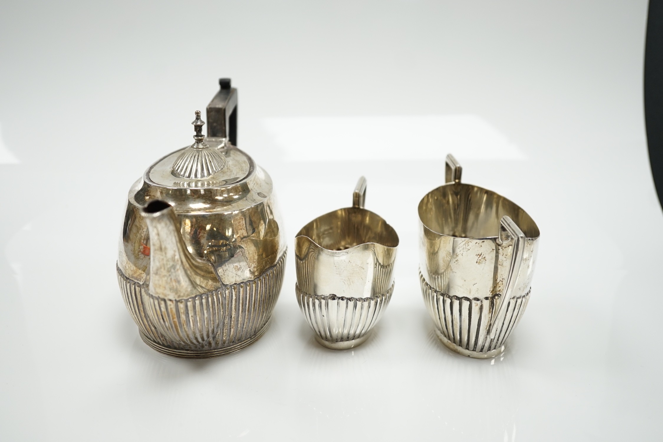 A matched early 20th century silver bachelor's three piece tea set, tea pot, James Dixon & Sons, Sheffield, 1920, cream and sugar, Walker & Hall, Sheffield, 1904, gross weight 14oz.